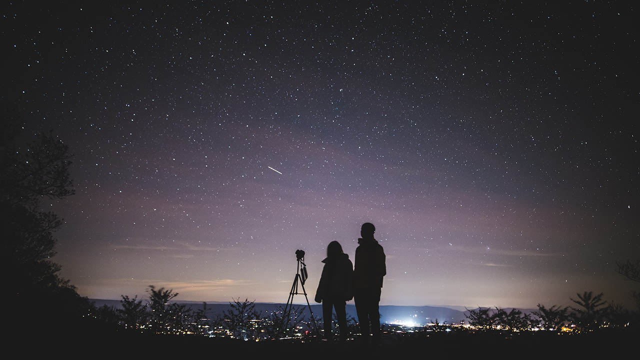 A silhouette of two people next to a telescope on a starry night, ready to observe the cosmos.